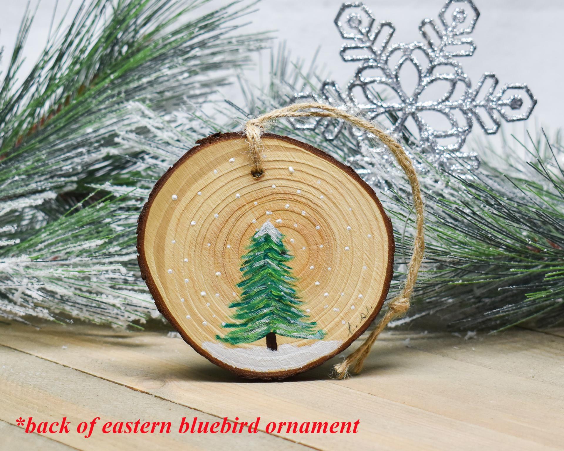 A hand-painted evergreen tree on the back of an eastern bluebird ornament at covecreekphotography.com.