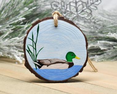 A wood slice Christmas ornament with a hand-painted mallard drake on a pond at Cove Creek Photography.