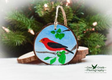 A handmade Christmas ornament with a scarlet tanager hand-painted on a wood slice available at Cove Creek Photography.