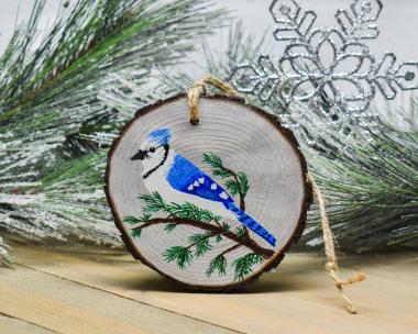 A blue jay on a cedar limb that is hand-painted on a wood slice ornament at Cove Creek Photography.