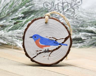An eastern bluebird in the snow hand-painted on a wood slice Christmas ornament at Cove Creek Photography.