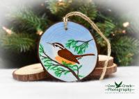A hand-painted wood slice ornament with a Carolina wren on a pine branch at Cove Creek Photography.