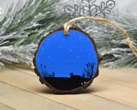 A wood slice with a hand-painted starry night sky and silhouettes of a loon on water and cattails at Cove Creek Photography.