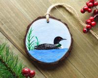 A hand-painted common loon wood slice Christmas ornament displayed on a weathered board at covecreekphotography.com.