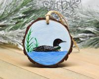 A wood slice Christmas ornament with a hand-painted common loon on blue water available at covecreekphotography.com.