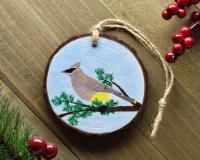 A handmade wood slice ornament with a hand-painted bird that is displayed on weathered wood at covecreekphotography.com.