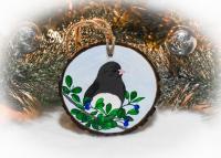 A hand-painted dark-eyed junco amid leaves and berries on a wood slice Christmas ornament at covecreekphotography.com.