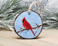 A red cardinal on a snow dusted branch with a sky background that is hand-painted on a wood round at Cove Creek Photography.