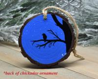 A silhouette of a bird perched on a branch and a starry night sky hand-painted on a wood slice at Cove Creek Photography.