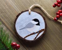 A hand-painted Carolina chickadee wood slice Christmas ornament displayed on weathered wood at covecreekphotography.com.