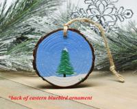 A hand-painted evergreen tree in the snow that was hand-painted on the back of a bluebird Christmas ornament at covecreekphotography.com.