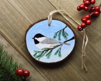 An acrylic painting on a wood slice with a chickadee perched on a limb at Cove Creek Photography.