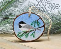 A Carolina chickadee perched on an evergreen limb is hand-painted on a wood slice Christmas ornament at Cove Creek Photography.