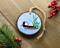 A handmade male hood merganser wood slice Christmas ornament displayed on a flat board at covecreekphotography.com.