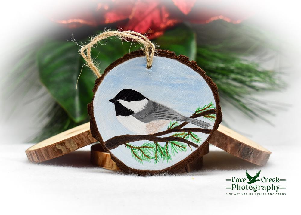 A wood slice Christmas ornament with a hand-painted Carolina chickadee available at www.covecreekphotography.com.