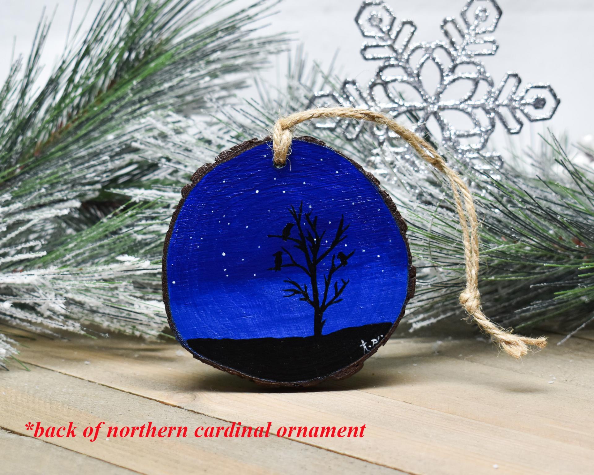 A deep blue starry night with a silhouette of birds perched in a tree is hand-painted on a wood slice ornament at Cove Creek Photography.