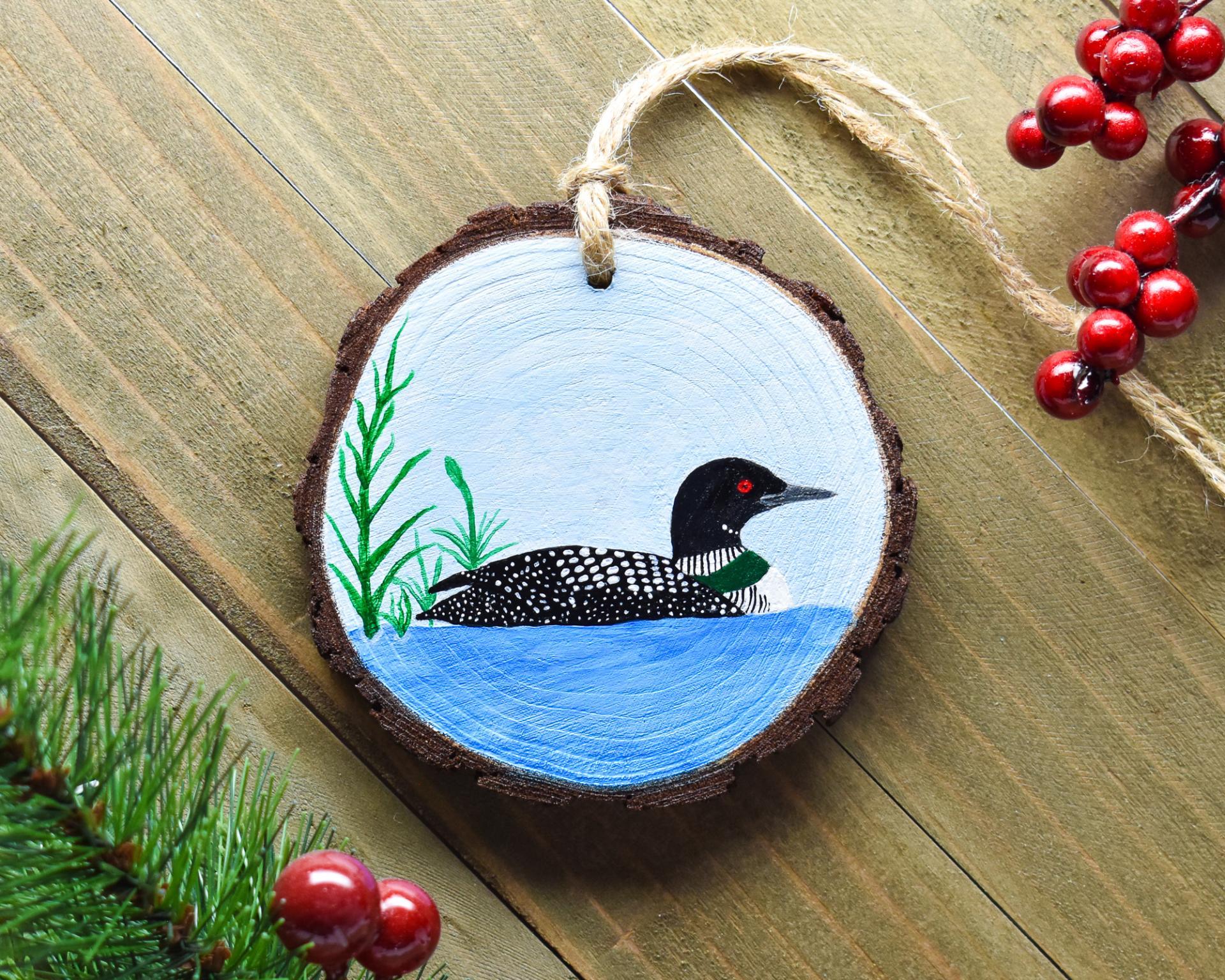 A hand-painted common loon wood slice Christmas ornament displayed on a weathered board at covecreekphotography.com.