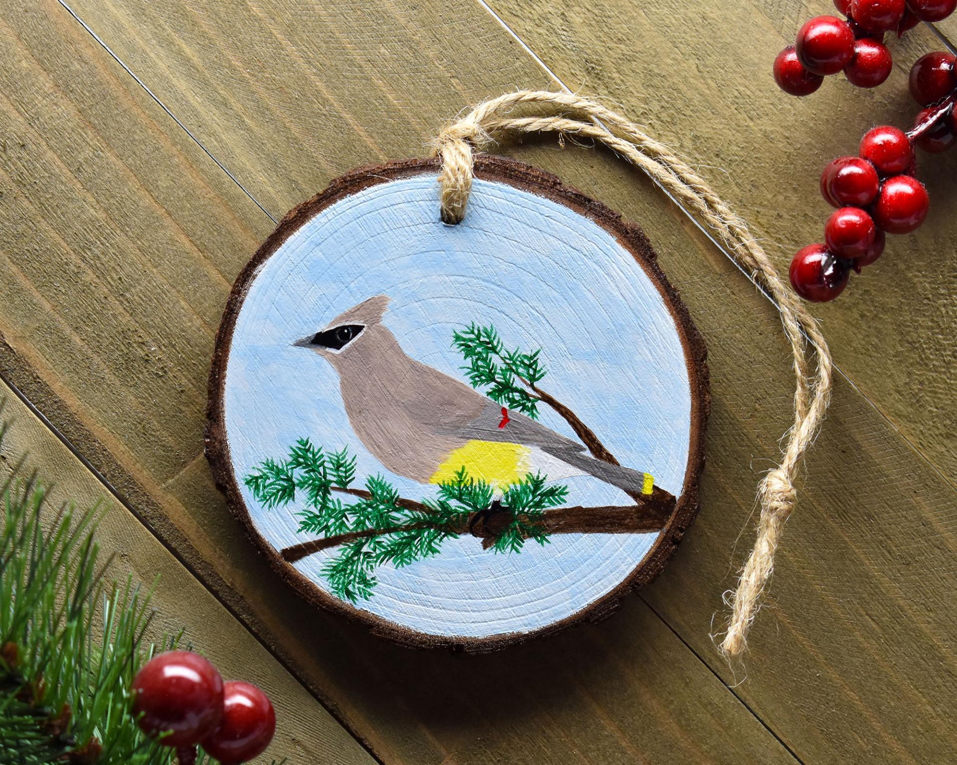 A handmade wood slice ornament with a hand-painted bird that is displayed on weathered wood at covecreekphotography.com.