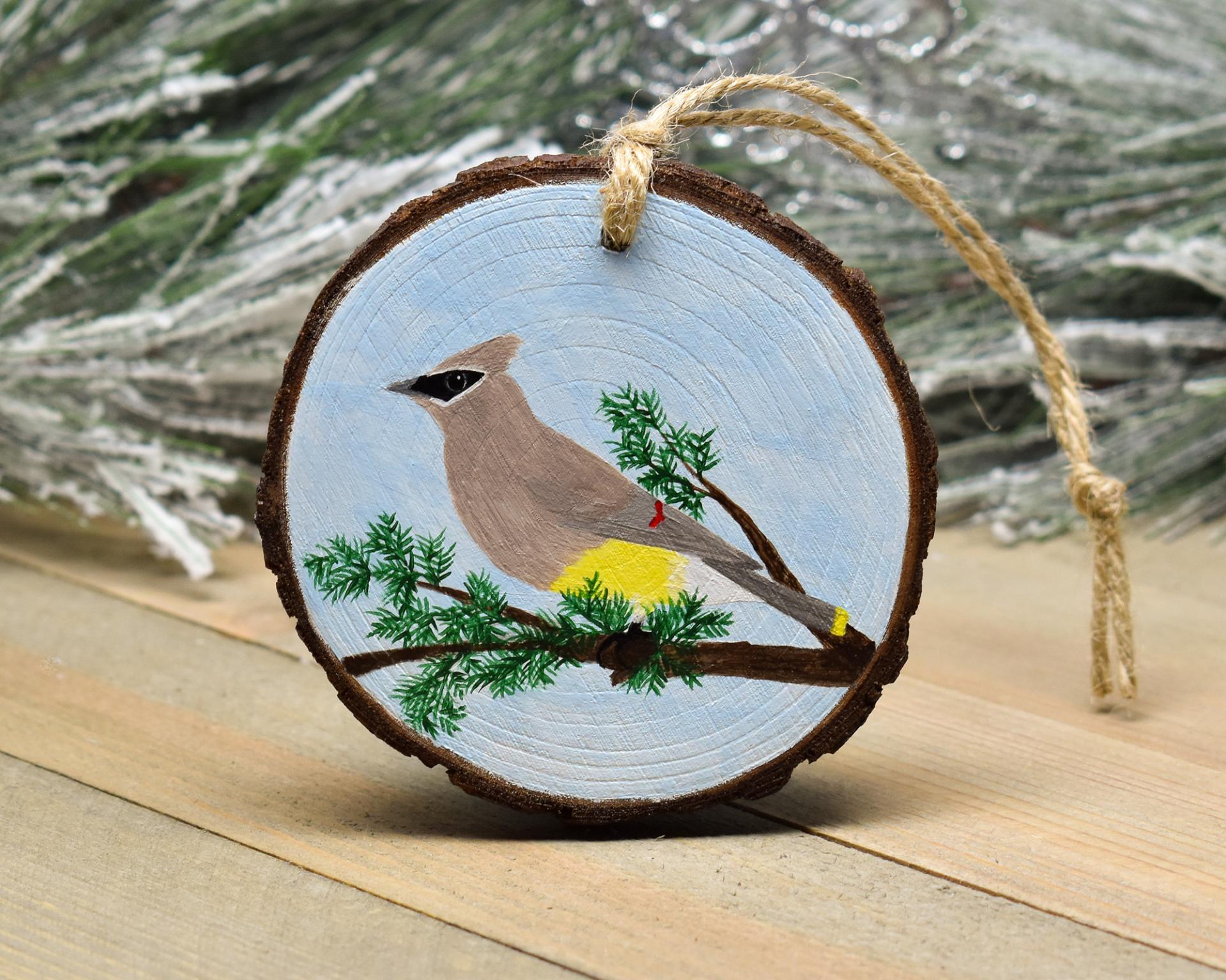 A hand-painted wood slice Christmas ornament with a cedar waxwing perched on a tree limb at Cove Creek Photography.