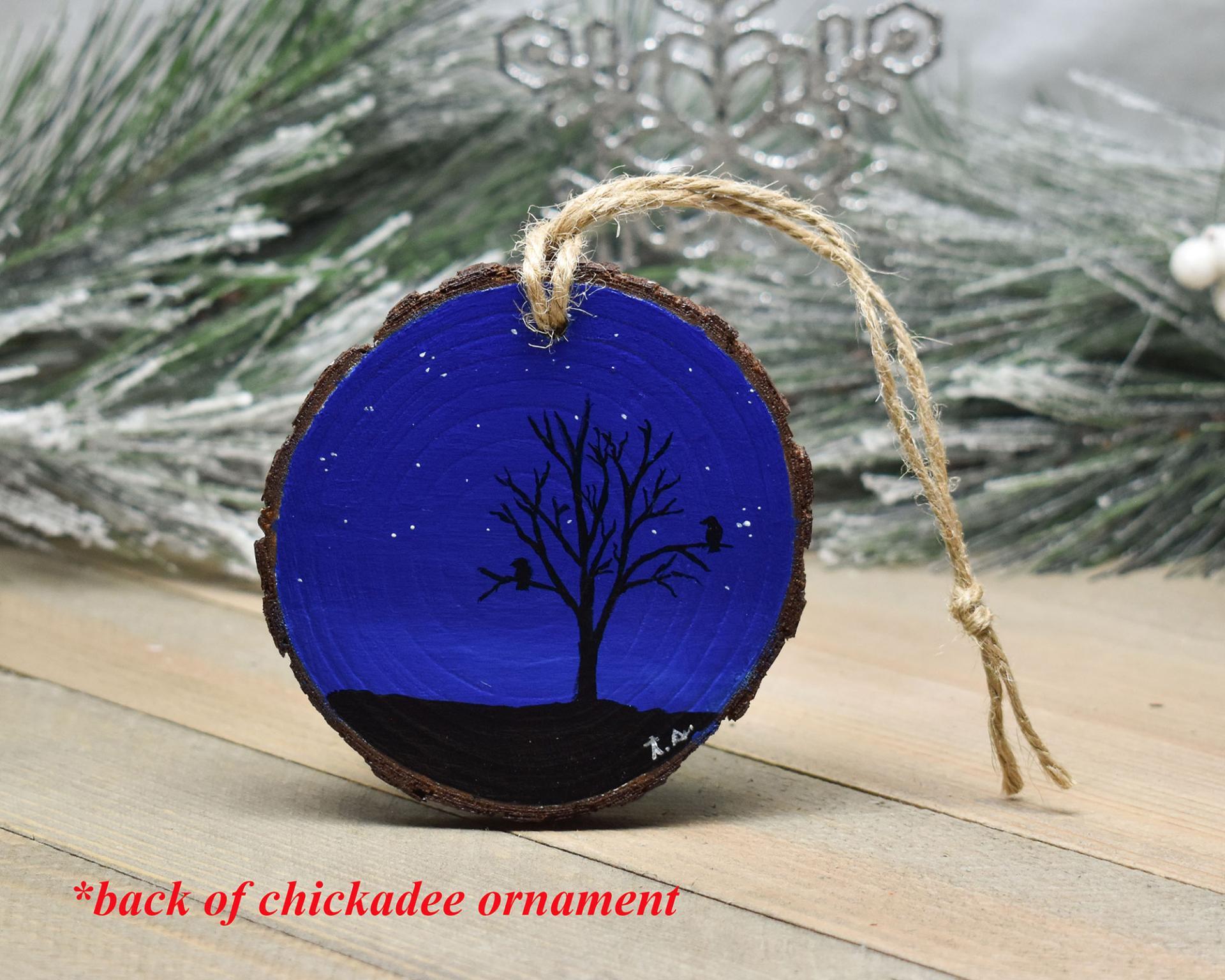 A starry night sky with tree and bird silhouettes hand-painted on a 3 inch wood slice at Cove Creek Photography.