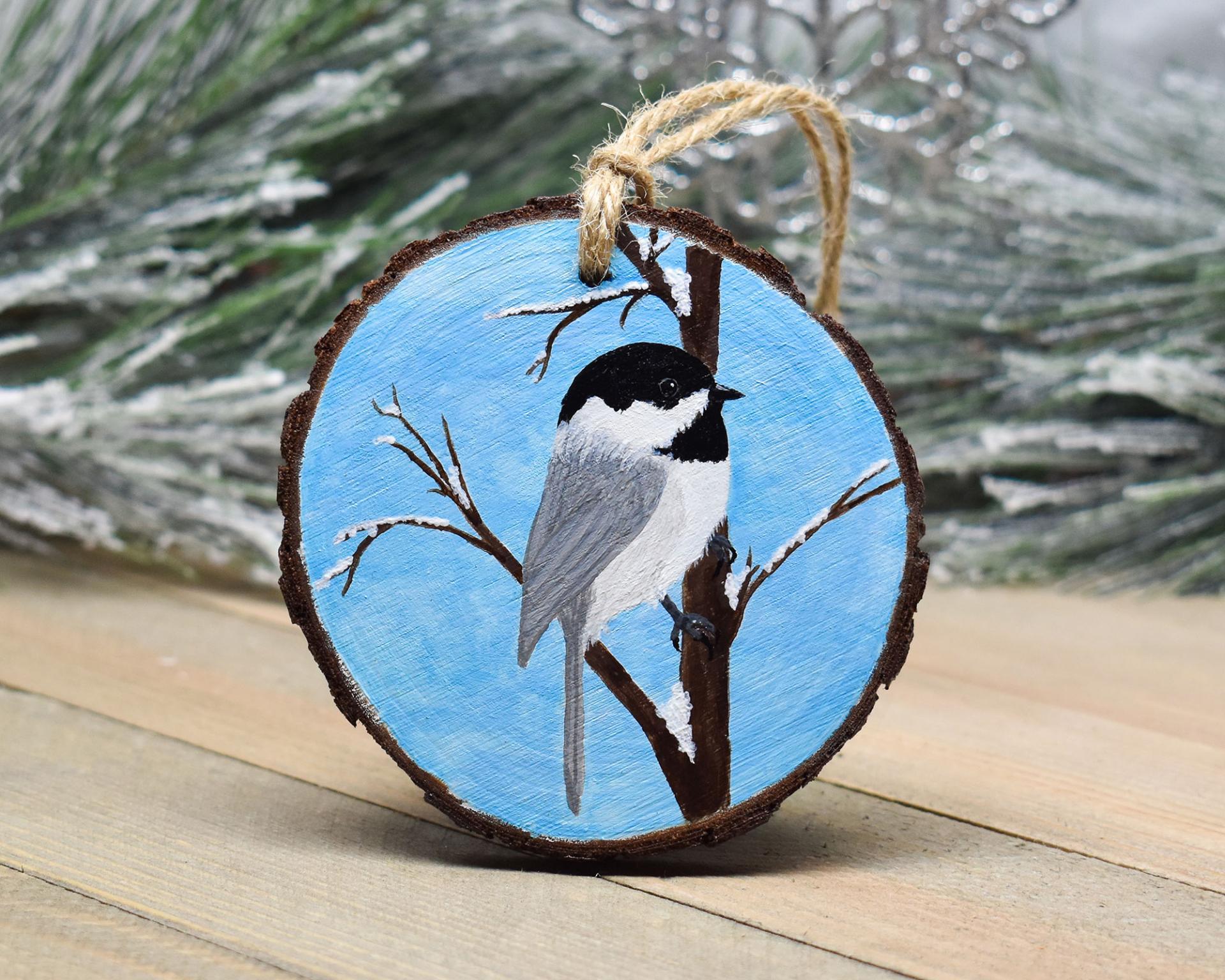 A chickdee perched amid snow covered branches hand-painted on a 3 inch wood slice at covecreekphotography.com.