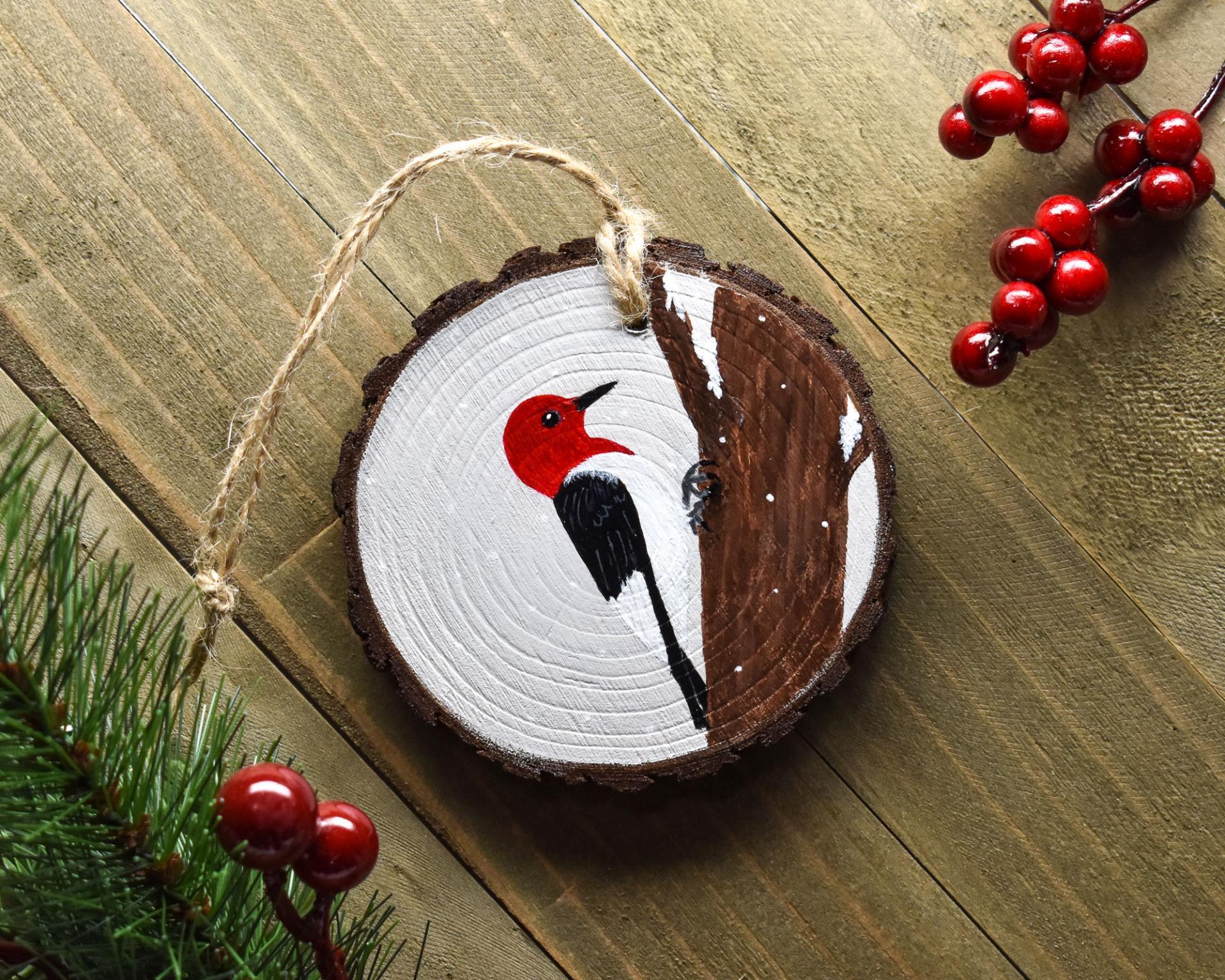 An acrylic painting of a woodpecker on the side of a tree featured on a wood slice Christmas ornament at covecreekphotography.com.