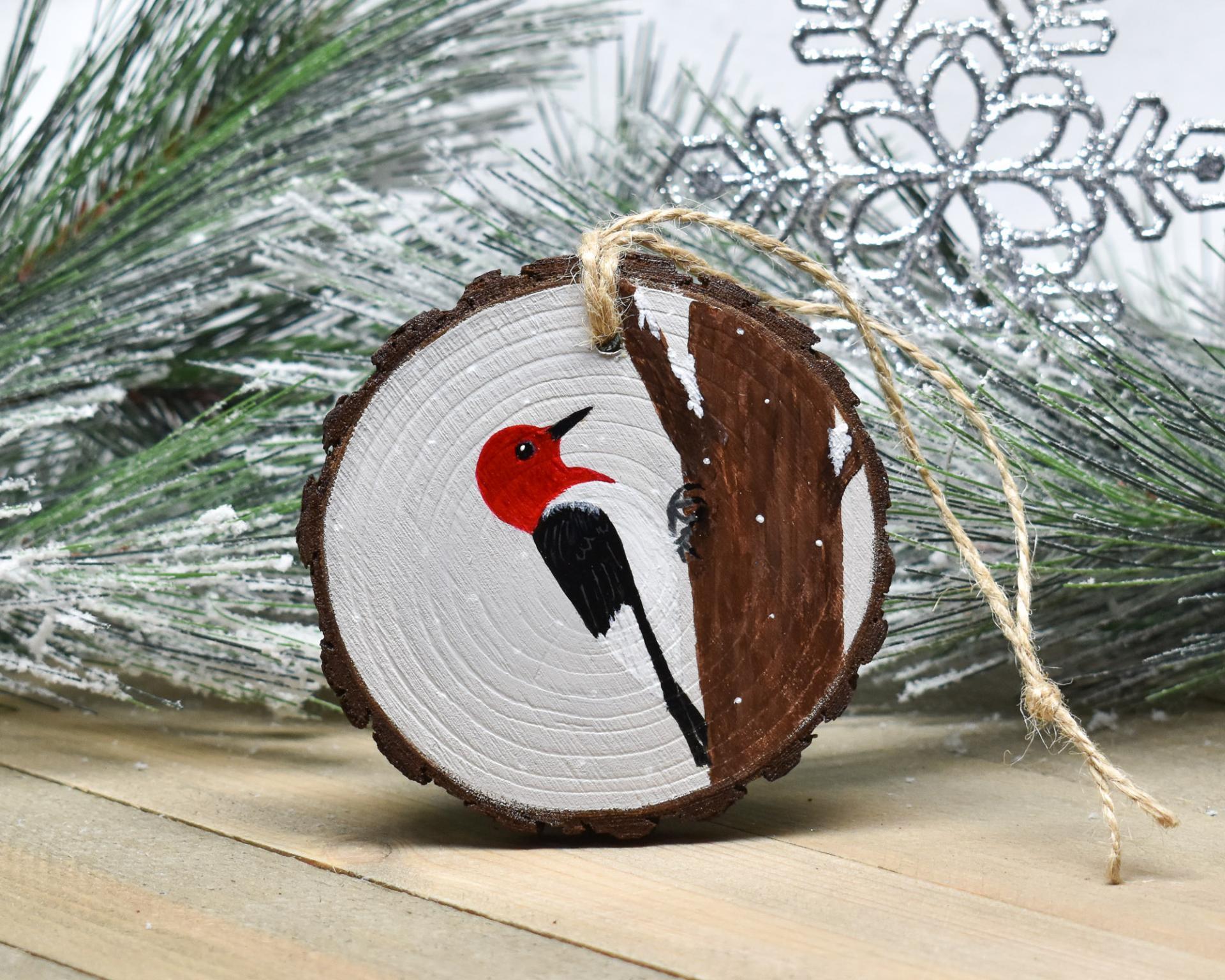 A hand-painted red-headed woodpecker on a wood slice ornament at Cove Creek Photography.
