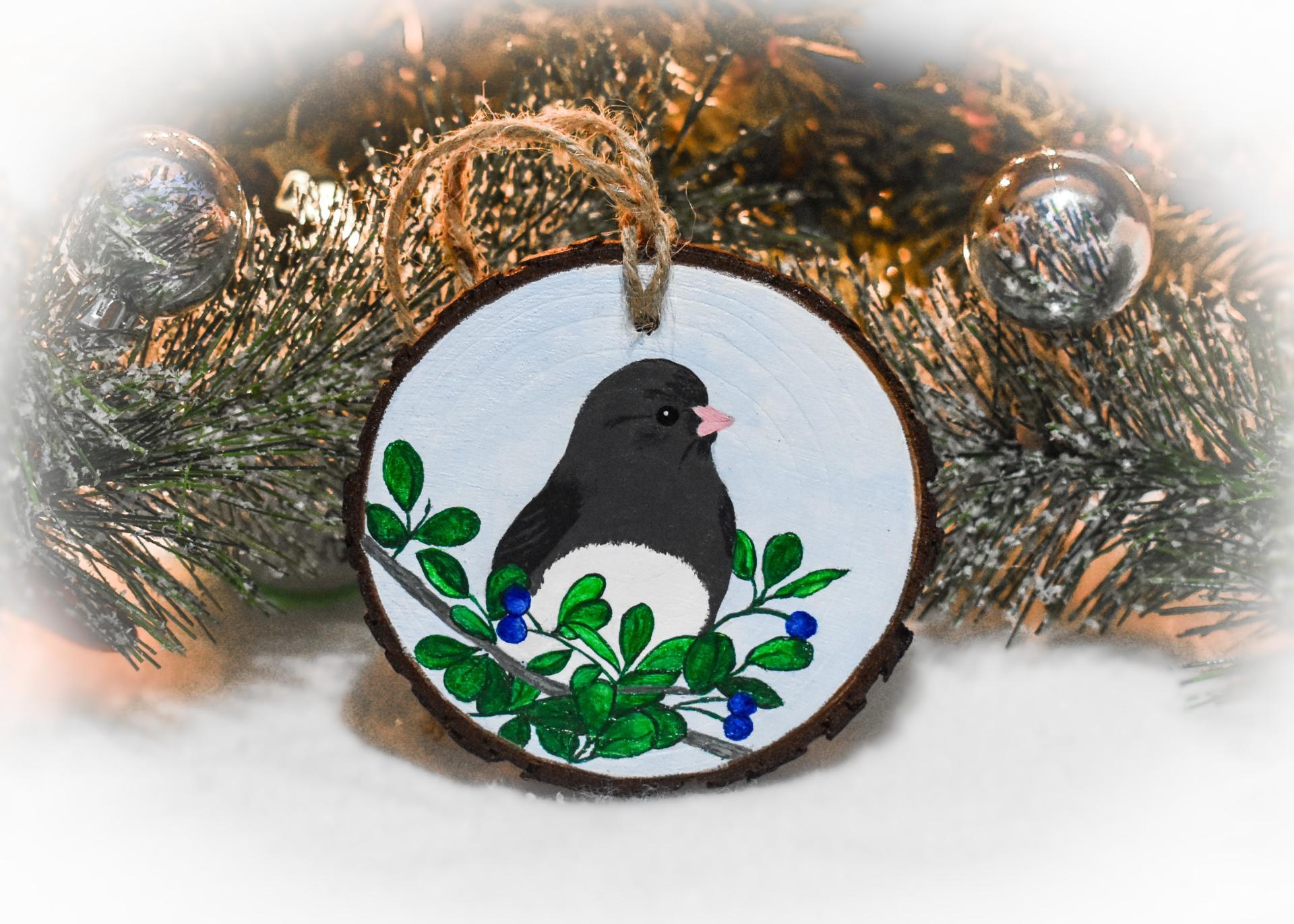 A hand-painted dark-eyed junco amid leaves and berries on a wood slice Christmas ornament at covecreekphotography.com.