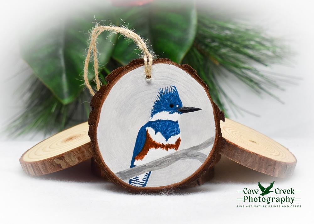 A hand-painted wood slice Christmas ornament with a belted kingfisher available for purchase at www.covecreekphotography.com.