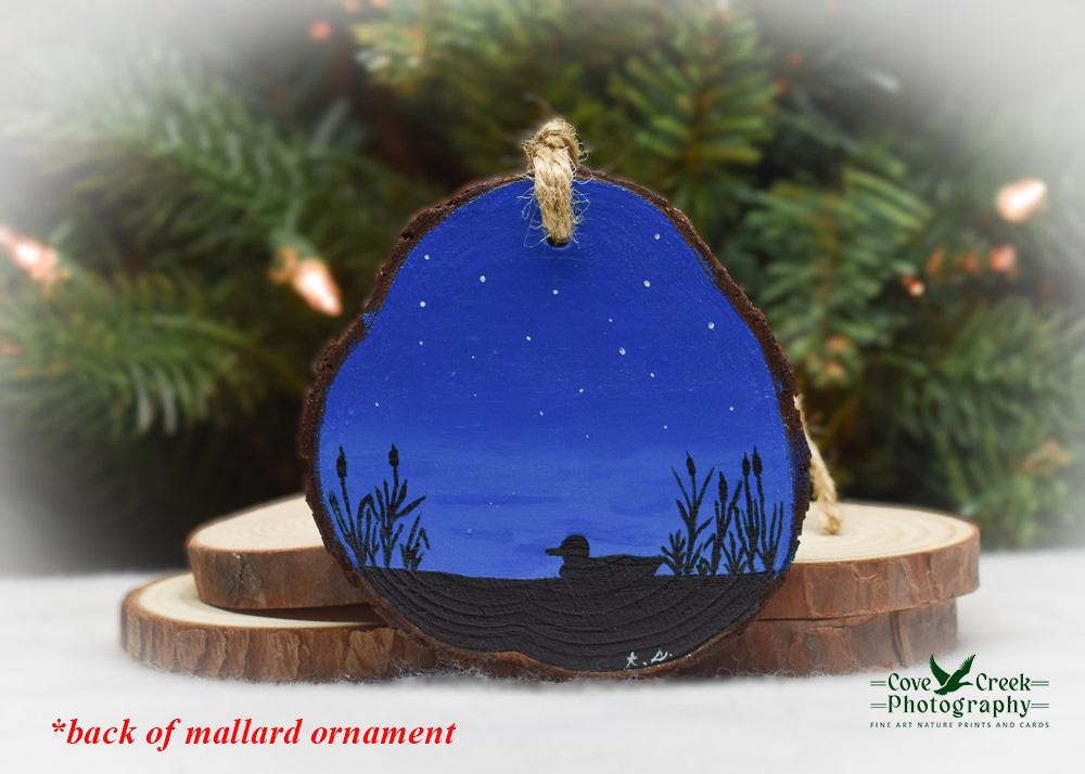 A hand-painted silhouette of a mallard in a marsh on wood slice Christmas ornamet at covecreekphotography.com.