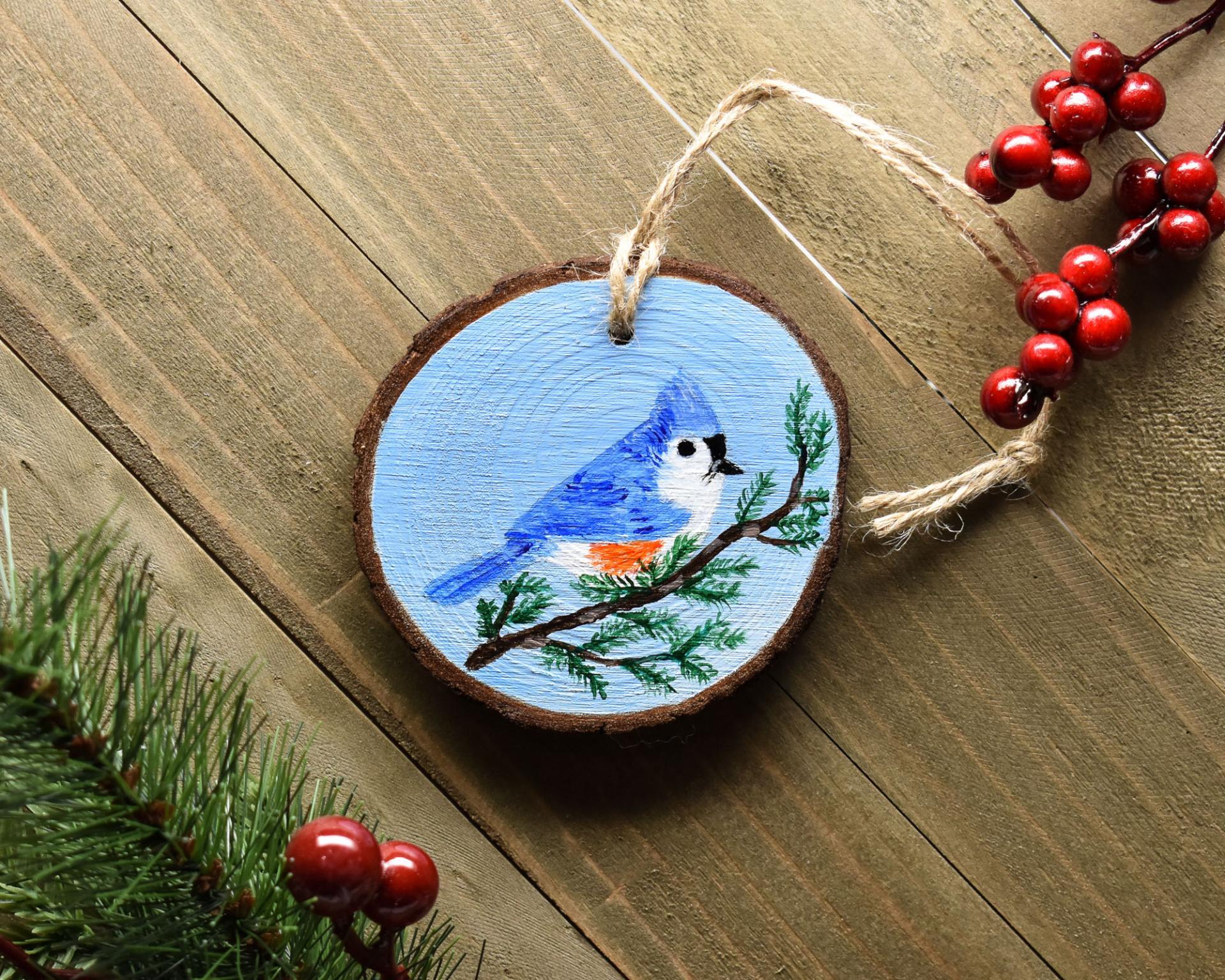 A hand-painted tufted titmouse wood slice Christmas ornament displayed on a wood background at covecreekphotography.com.