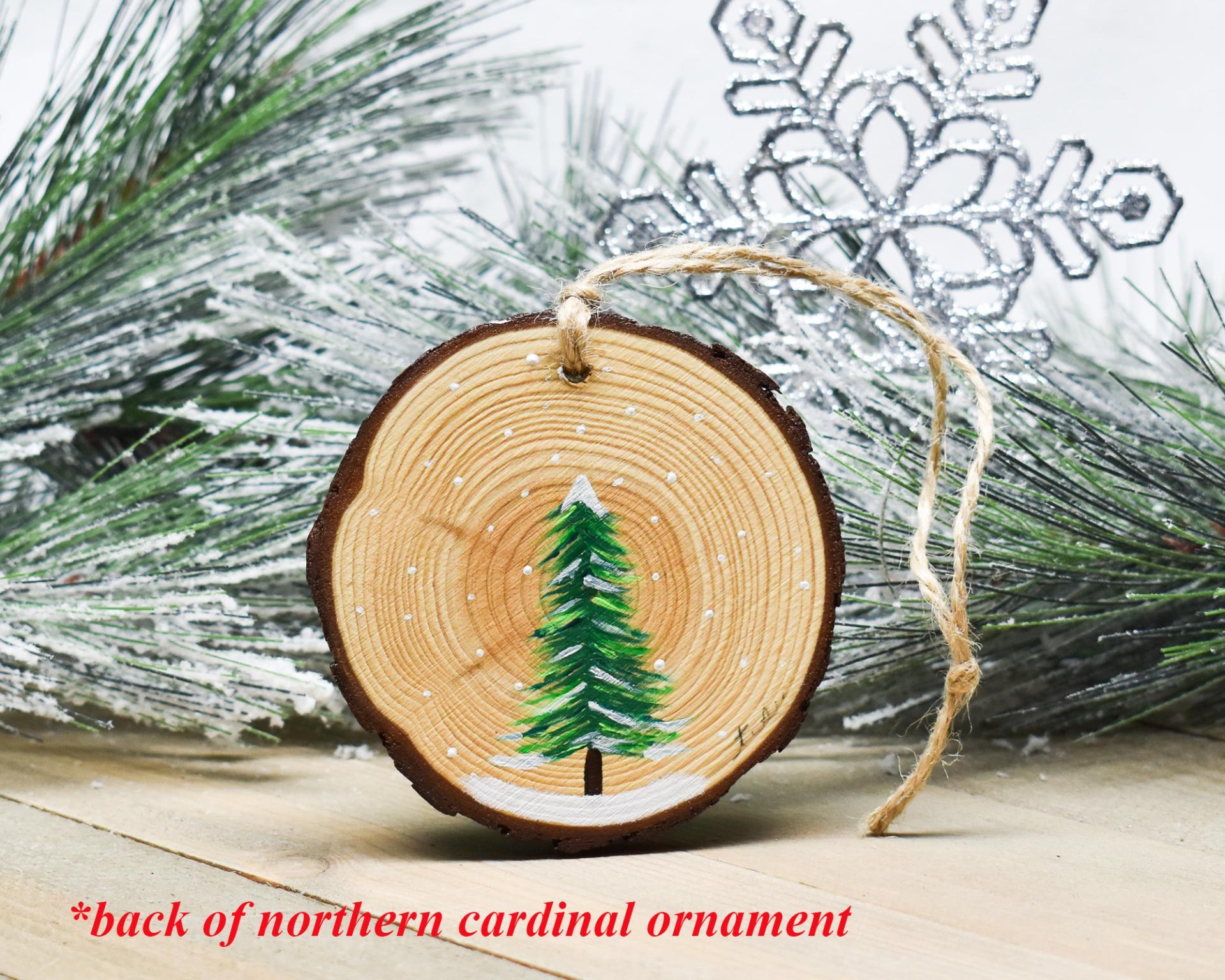 An evergreen tree in the snow hand-painted on the back of a northern cardinal ornament at covecreekphotography.com.