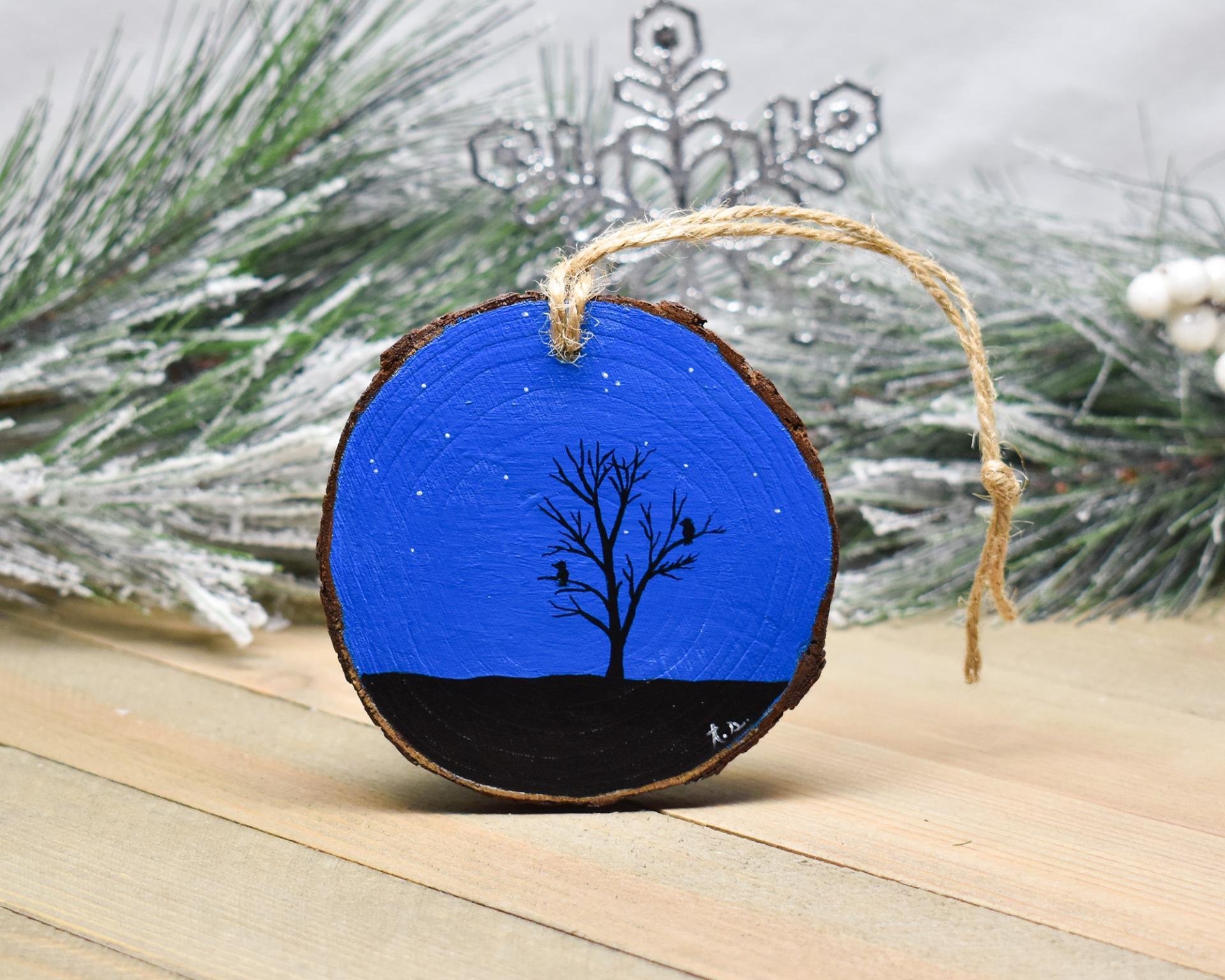 A hand-painted wood slice ornament with a night sky and bird and tree silhouettes at covecreekphotography.com.