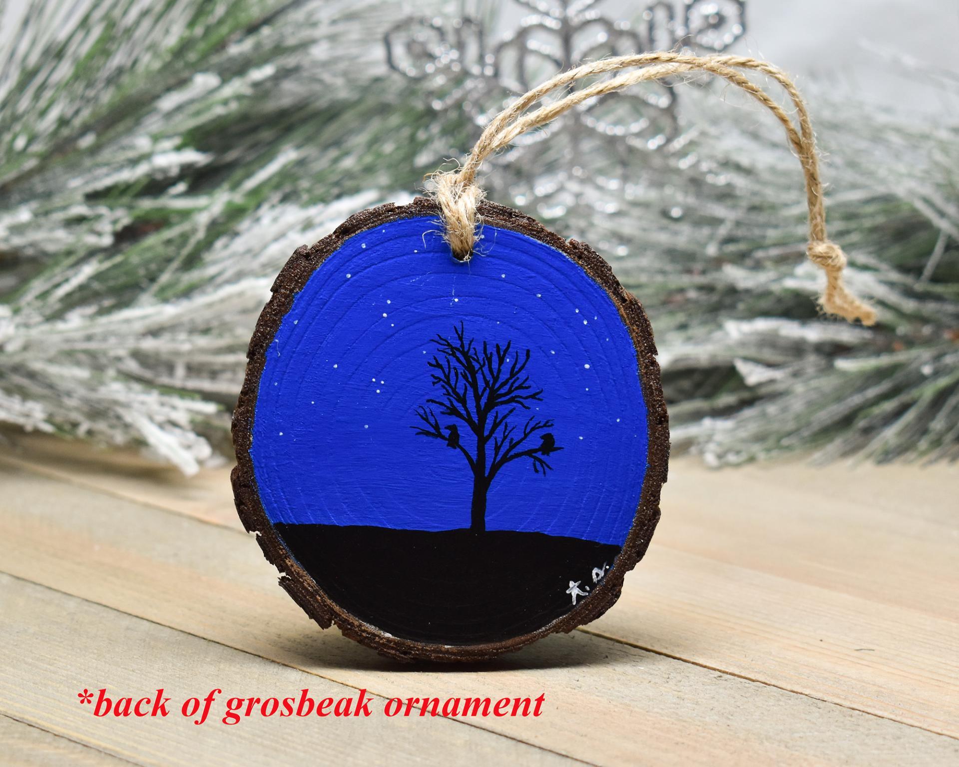 An ornament with a hand-painted silhouette of a tree and birds against a dark blue starry background at Cove Creek Photgraphy.