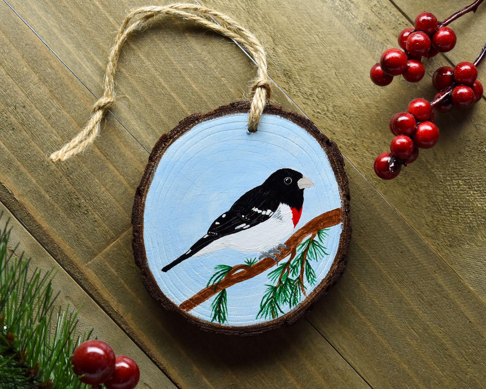 A hand-painted rose-breasted grosbeak wood slice Christmas ornament display on weathered wood at covecreekphotography.com.