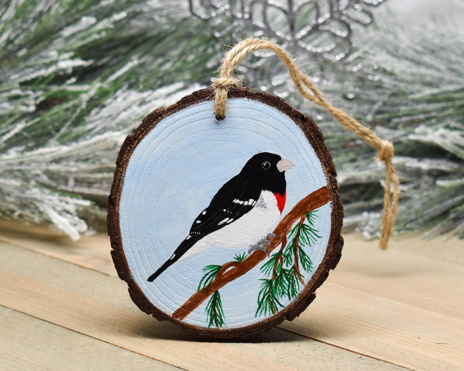 A three inch diameter wood slice Christmas ornament with a hand-painted rose-breasted grosbeak at Cove Creek Photography.
