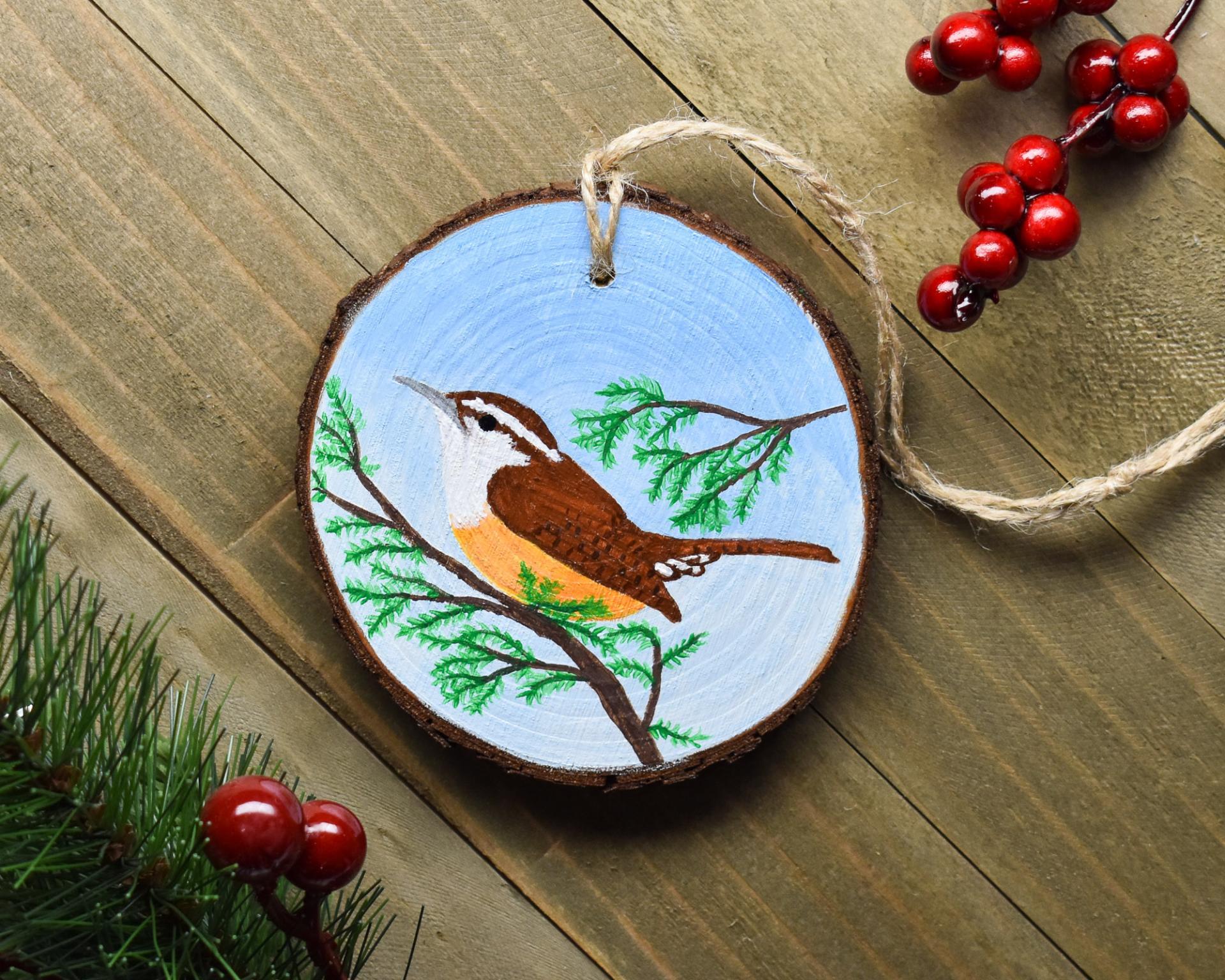 A handmade wood slice Christmas ornament with a hand-painted Carolina wren at Cove Creek Photography.
