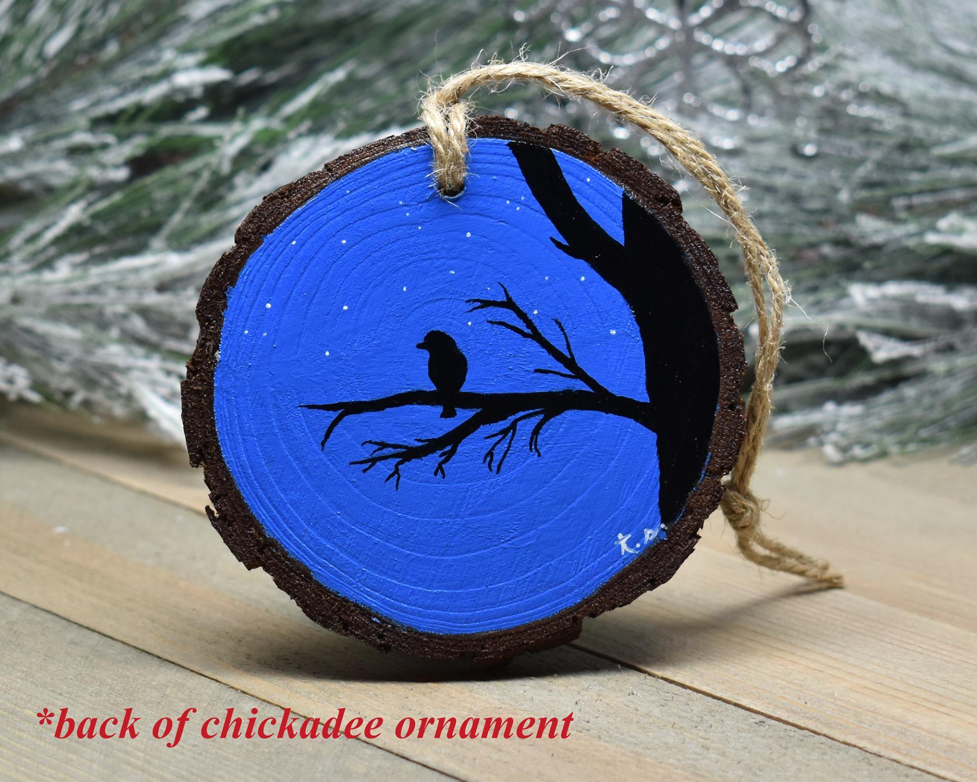 A silhouette of a bird perched on a branch and a starry night sky hand-painted on a wood slice at Cove Creek Photography.
