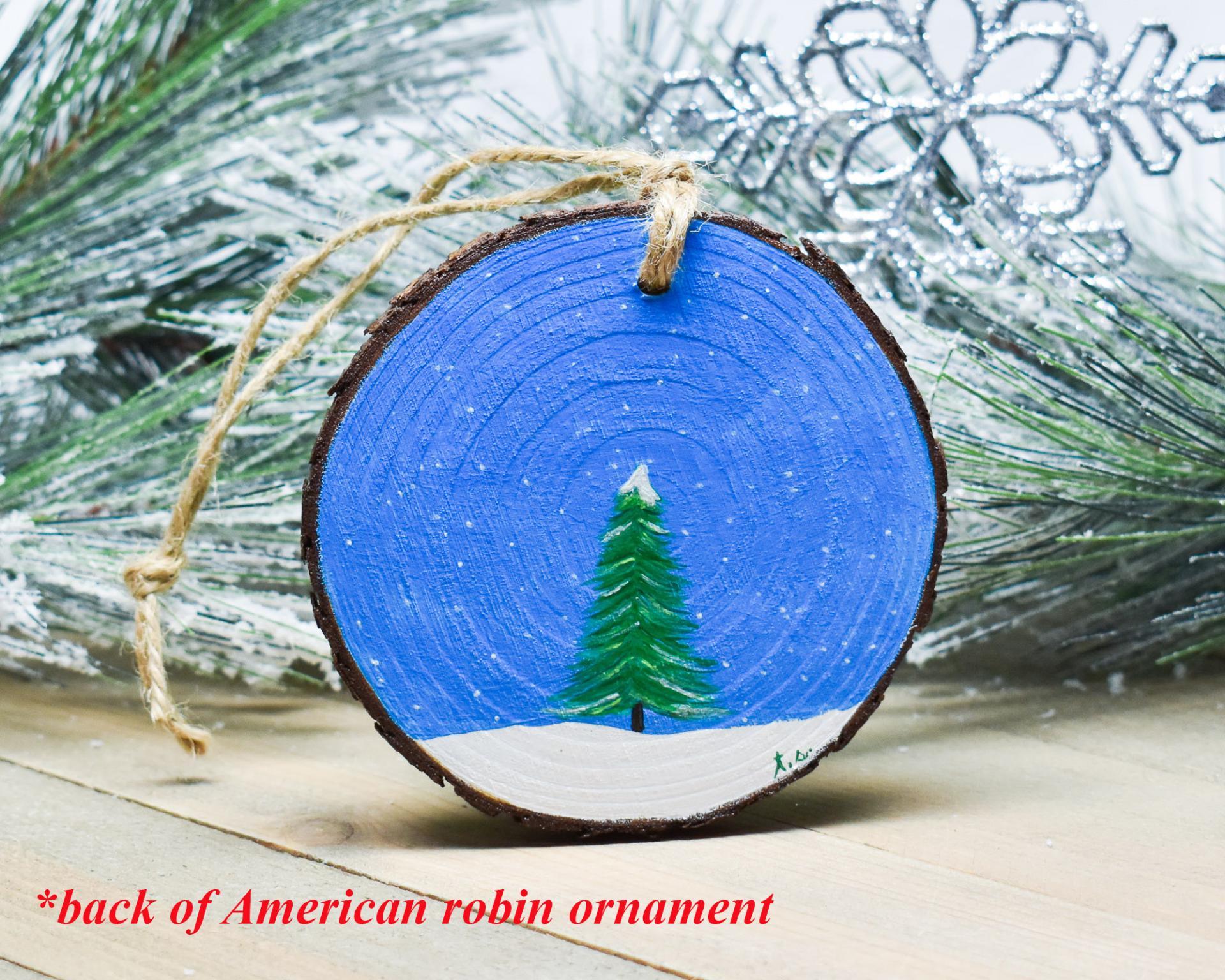 An evergreen tree in the snow that is hand-painted on the back of an American robin wood slice ornament at covecreekphotography.com.