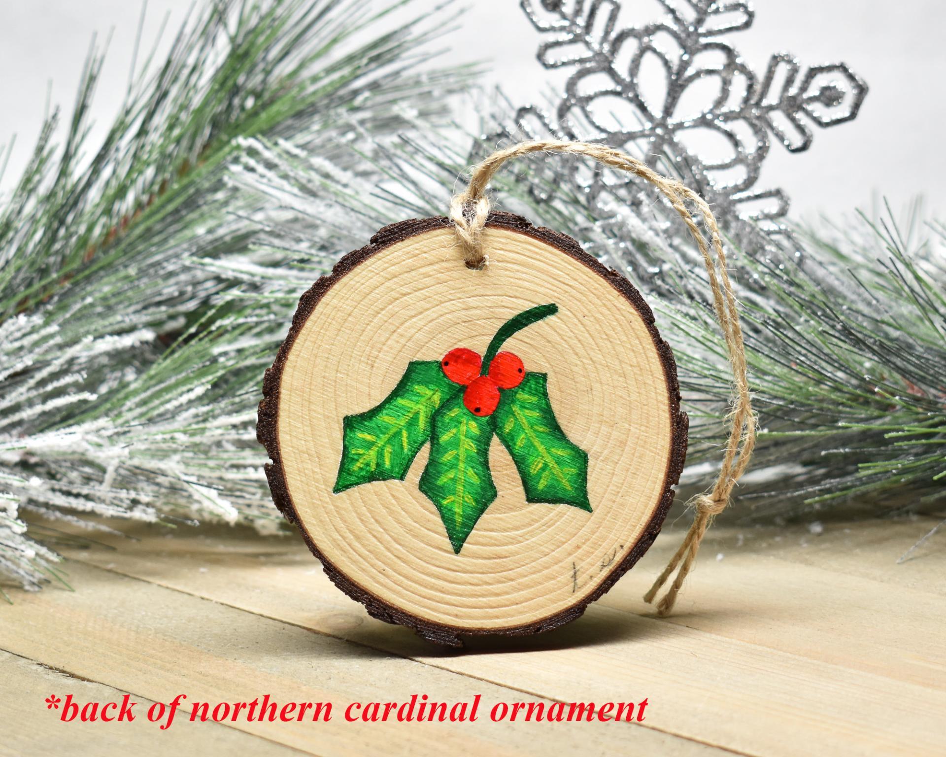 The holly leaves with three red berries hand-painted on the back of a handmade northern cardinal ornament at Cove Creek Photography.