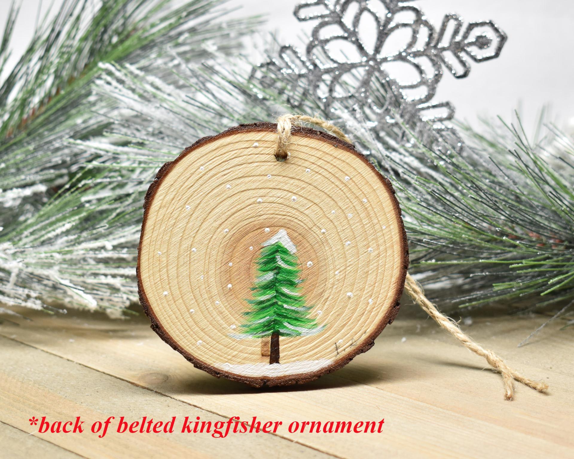 A simple hand-painted rendering of an evergreen tree in snow on a wood slice ornament at Cove Creek Photography.