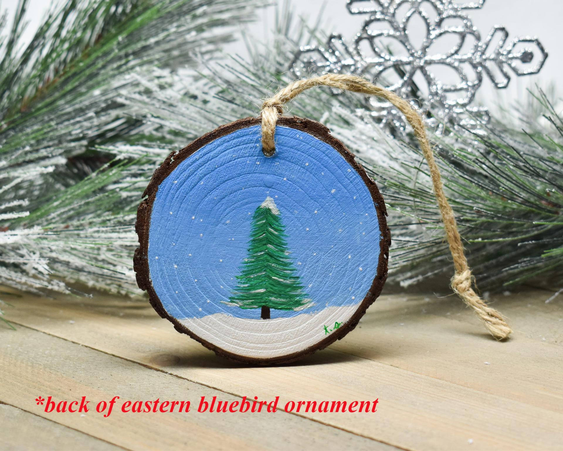 A hand-painted evergreen tree in the snow that was hand-painted on the back of a bluebird Christmas ornament at covecreekphotography.com.
