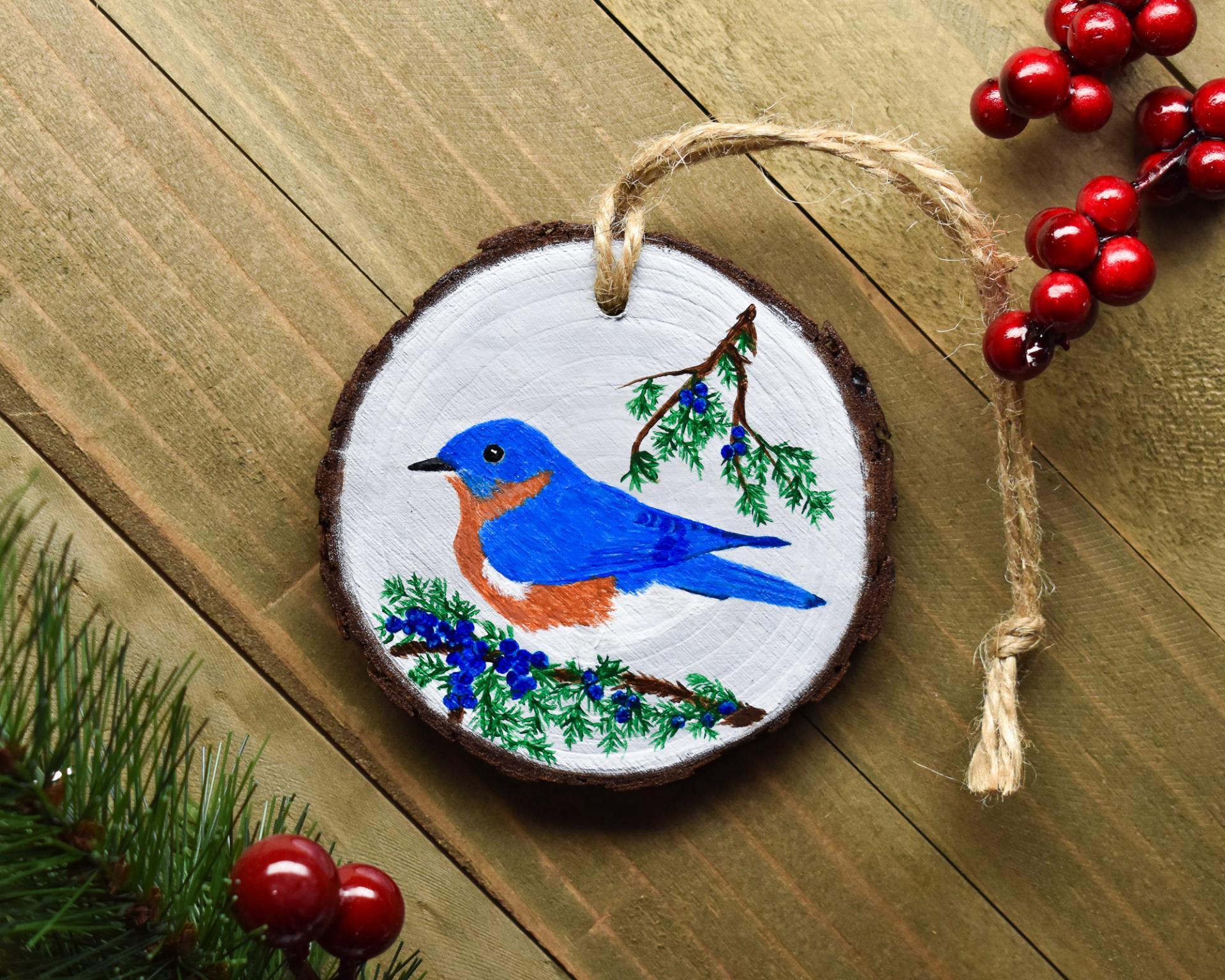 A wood slice with a hand-painted bluebird perched amid cedar limbs at covecreekphotography.com.