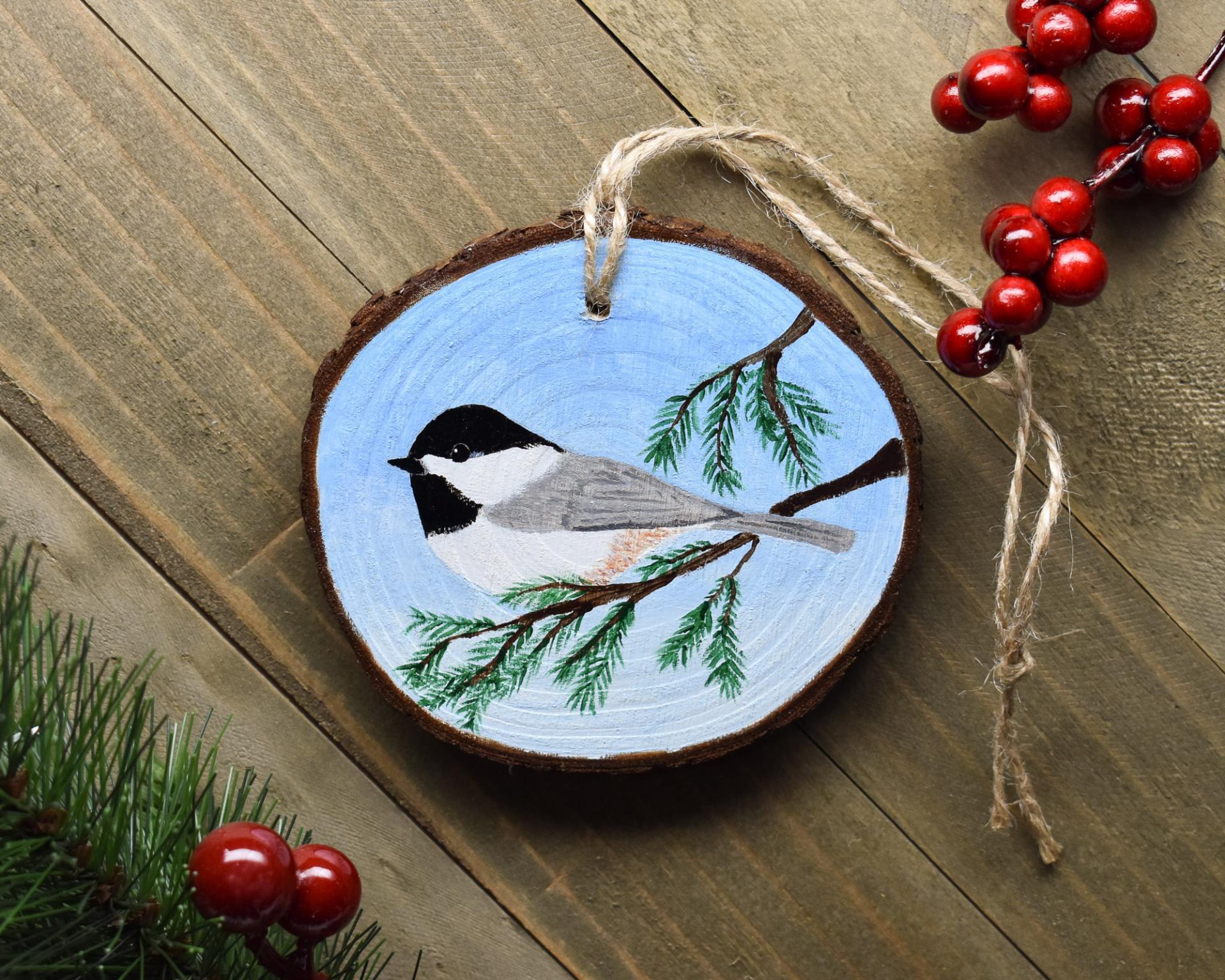An acrylic painting on a wood slice with a chickadee perched on a limb at Cove Creek Photography.
