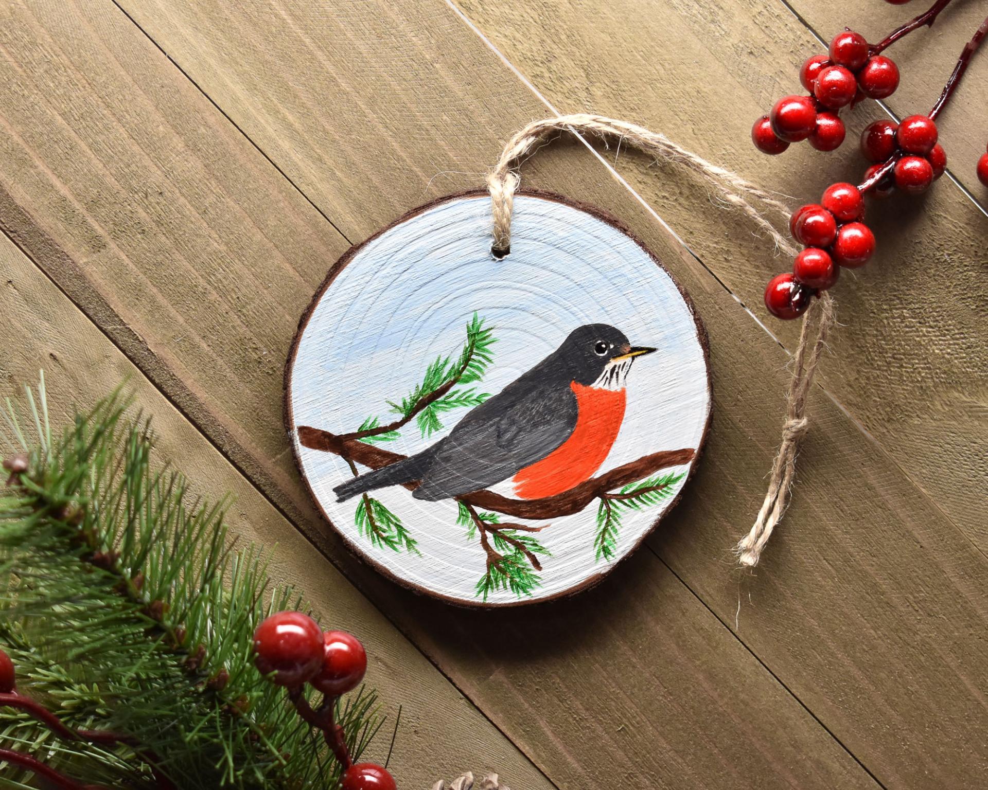 A hand-painted American robin Christmas ornament displayed on a flat wood surface at Cove Creek Photography.