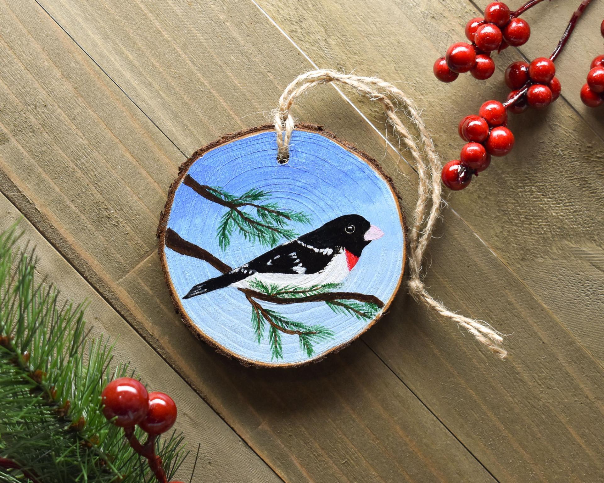 A male rose-breasted grosbeak hand-painted onto a wood slice ornament at Cove Creek Photography.