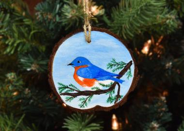 A hand-painted eastern bluebird wood slice ornament hanging on a Christmas tree at www.covecreekphotography.com.