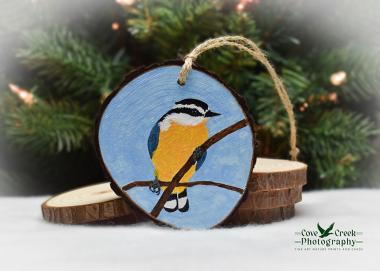 An acrylic painting of a red-breasted nuthatch on a 3.5 inch wood slice Christmas ornament at Cove Creek Photography.